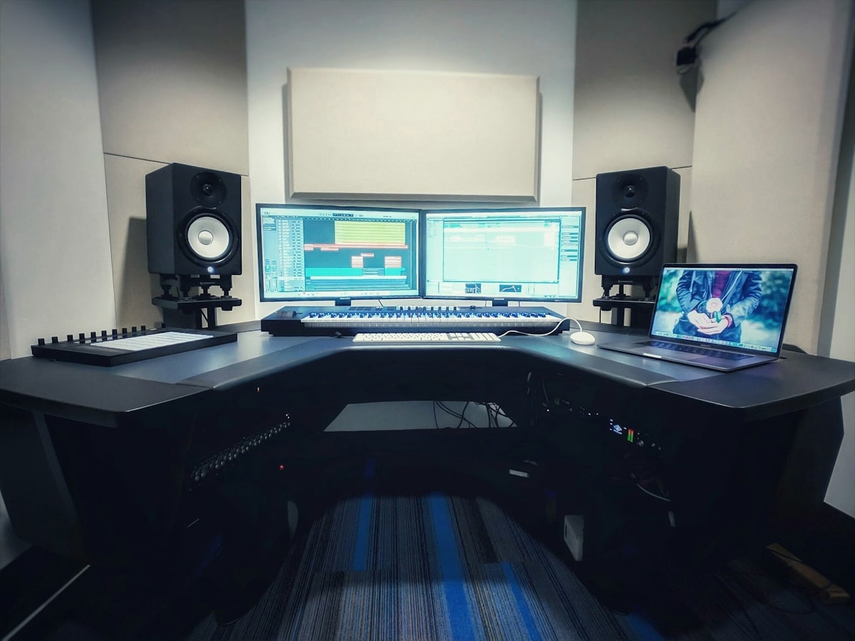 Dan's studio desk with dual monitors running a DAW session, a MIDI keyboard controller, and studio monitors